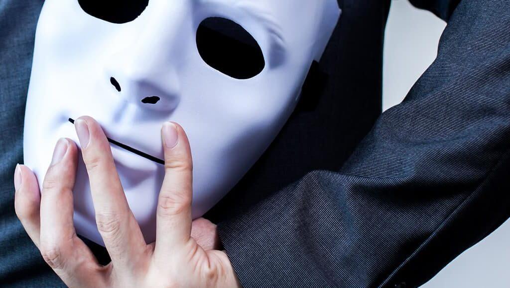 Understanding Identity Fraud: How to Protect your Company Directors image - man wearing dark clothing hiding a white mask behind his back